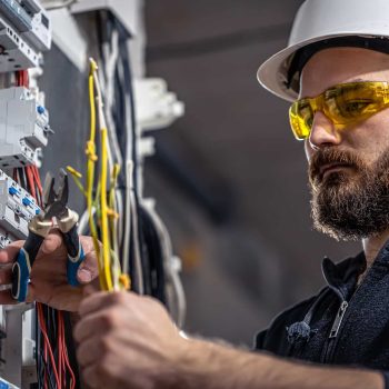 male-electrician-works-switchboard-with-electrical-connecting-cable-min